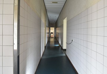 <p>Overzicht van de middengang in het zuidelijk deel van de westvleugel. Met uitzondering van de gangen langs de manschappenkamers, zijn de (overige) gangen voorzien van een hoge lambrisering van witte ceramische tegels. </p>
